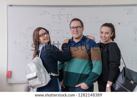 group portrait of young students standing in front of white chalkboard and looking at the camera