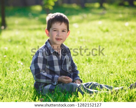 Beautiful little brunet hair boy, has pretty face, happy eyes, dressed in blue plaid shirt, play in garden. Child family portrait. Creative concept. Summer time. Close up.