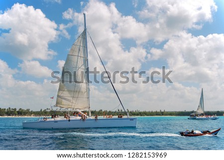 Catamaran with big white sails in a tropical sea near island with palm trees. Tour along coast.