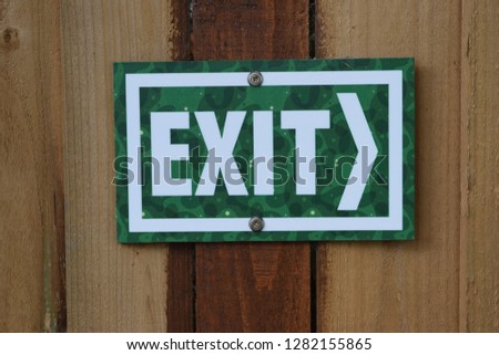 Bright green exit sign nailed on wooden post, blurred background 