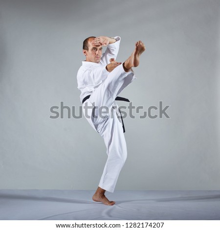 On a gray background, an athlete in karategi makes formal karate exercises