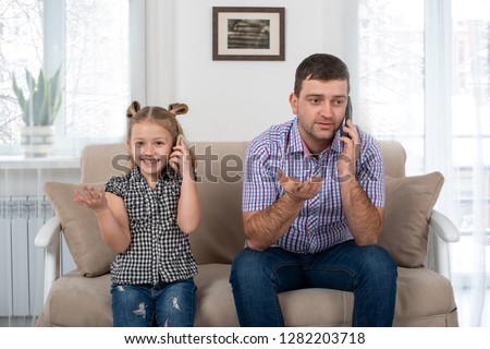 Studio shot of a daughter and dad sitting on the sofa at home and talking on the phone the same way.  Daughter imitates her father. Royalty-Free Stock Photo #1282203718