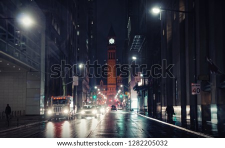 Night rainy Bay street view in downtown Toronto lit with cars` headlamps beams reflecting in wet asphalt with Toronto Old City Hall Clock Tower in background 