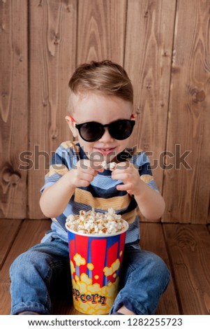Little cute kid baby boy 2-3 years old , 3d imax cinema glasses holding bucket for popcorn, eating fast food on wooden background. Kids childhood lifestyle concept. Copy space.