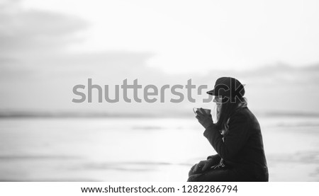 Beautiful girl is drinking hot coffe from the thermos for a walk. How to warm up in winter or autumn and overcome depression. Black and white photo.