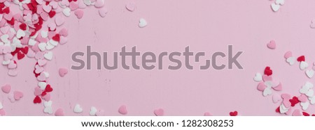 Panoramic website banner image with many tiny heart-shaped sugar sprinkles in red, white and pink with space for copy text or romantic love message for Valentine's Day on February 14th, flat lay
