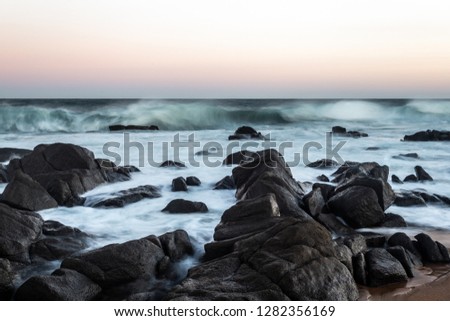 rocky beach with view of rough waves in a blue ocean with a purple, pink, orange blue sky taken from a low angle during sunset in South Africa