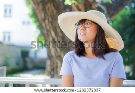 Portrait young beautiful Asian woman wearing eyes glassess and straw hat and sitting in the garden. Copy space for text.