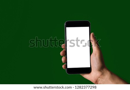 Hand holding white mobile phone with blank white screen green background.