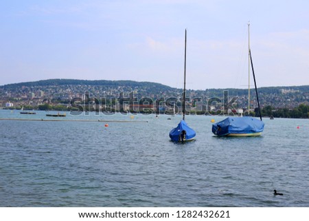 Beautiful landscape from Lake Zürich area in Zürich, Switzerland. In this photo you can see two small sail boats, blue sky and the mountains of Switzerland. Photographed during a summer day.