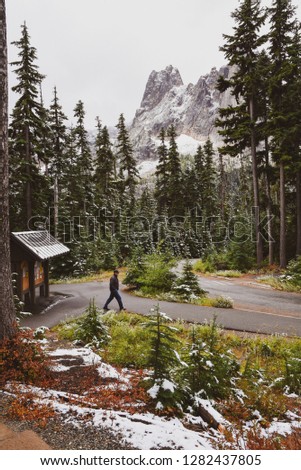 Man walking across recreation area at Washington Pass lookout  with forest, mountain and snow on ground