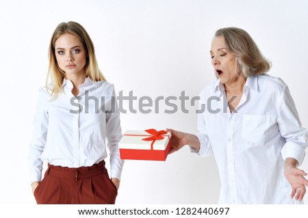 Angered elderly woman with a short haircut holds a gift box on her arm and a beautiful girl with a hurt look          