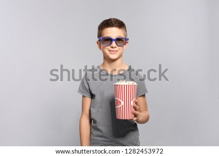 Boy with 3D glasses and popcorn during cinema show on grey background