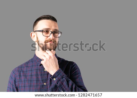 Young handsome man with facial hair holding posing over gray wall with a lot of copy space for text. Portrait of confident bearded male, wearing hipster slim fit checkered shirt. Isolated, background.