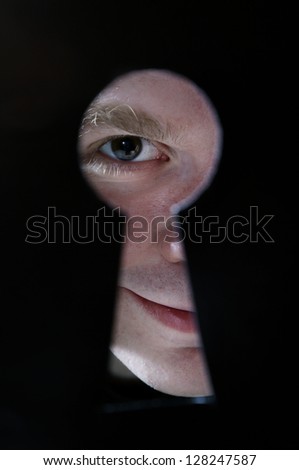 Man eye looking through hole in keyhole, on black background