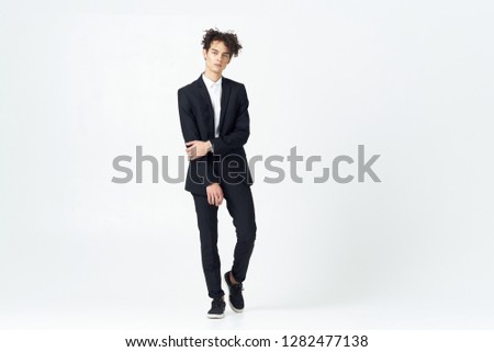business man with curly hair in a dark full-length suit on a light background                   