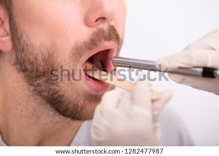 Close-up Of Doctor's Hand Examining Man's Throat With Tongue Depressor Royalty-Free Stock Photo #1282477987