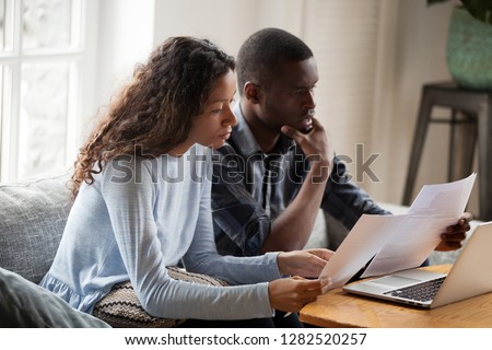 Serious worried african american couple reading documents consider mortgage loan insurance contract terms, focused black man and woman holding checking bank papers at home, domestic bills concept Royalty-Free Stock Photo #1282520257