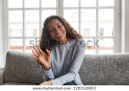 Happy friendly african american woman waving hand looking at camera sitting on couch, smiling mixed race millennial female vlogger making video call vlog at home, dating online, headshot portrait Royalty-Free Stock Photo #1282520851