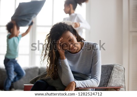 African american single mom feels headache sad depressed tired of noisy active 2 children playing at home, exhausted stressed black mother fatigued with upbringing difficult disobedient kids alone Royalty-Free Stock Photo #1282524712