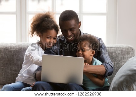 Happy african father and little daughter son using laptop doing family online shopping on sofa, black dad watching funny video with kids on computer, daddy and children having fun playing with app