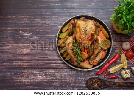 Roasted chicken, potatoes and vegetables in plate on dark wooden background. Top view. With copy space.