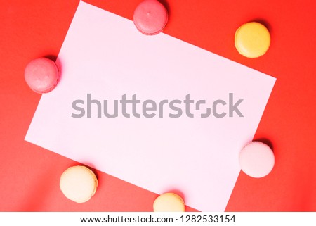 Closeup paper for copy space, text and advertising on red background with multicolored pink and yellow macaroons