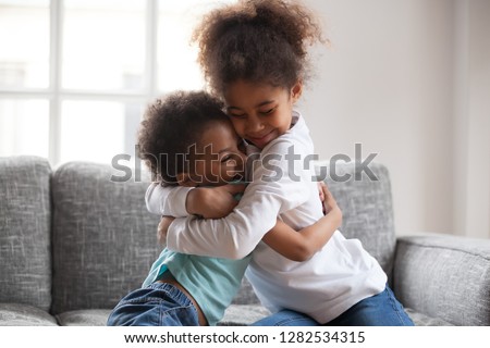 Cute happy african american siblings hugging cuddling feeling love and connection, smiling mixed race kid girl sister embracing little boy brother sitting on couch, 2 children good relationships Royalty-Free Stock Photo #1282534315