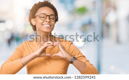 Young beautiful african american woman wearing glasses over isolated background smiling in love showing heart symbol and shape with hands. Romantic concept.