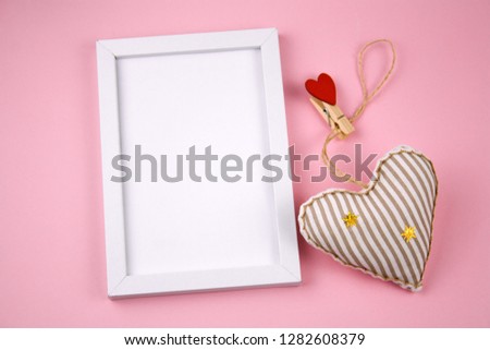 top view empty white wooden frame  and fabric soft toy in a shape of heart pastel pink background