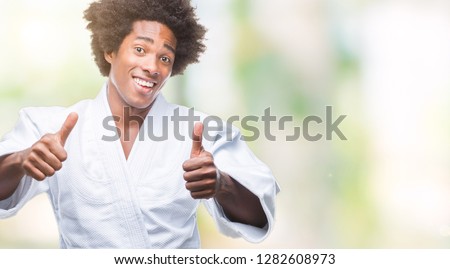 Afro american man wearing karate kimono over isolated background approving doing positive gesture with hand, thumbs up smiling and happy for success. Looking at the camera, winner gesture.