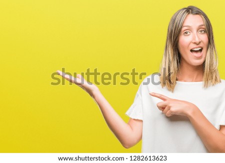 Young beautiful woman over isolated background amazed and smiling to the camera while presenting with hand and pointing with finger.