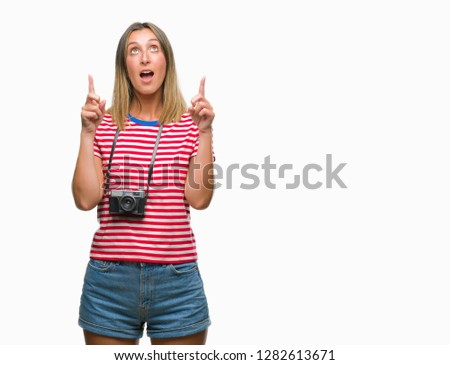 Young beautiful woman taking pictures using vintage photo camera over isolated background amazed and surprised looking up and pointing with fingers and raised arms.
