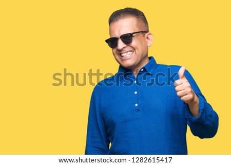Middle age arab man wearing sunglasses over isolated background doing happy thumbs up gesture with hand. Approving expression looking at the camera with showing success.