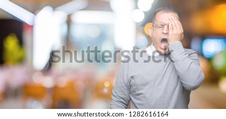 Middle age bussines arab man wearing glasses over isolated background Yawning tired covering half face, eye and mouth with hand. Face hurts in pain.