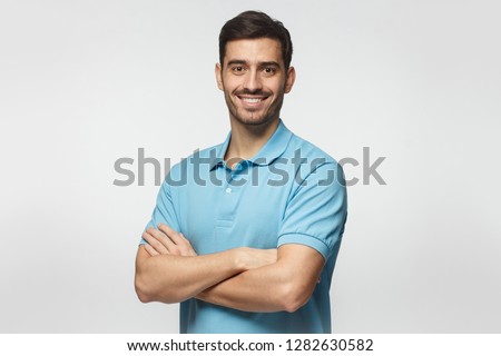 Portrait of young european caucasian man isolated on gray background, standing in blue polo shirt with crossed arms, smiling and  looking at camera Royalty-Free Stock Photo #1282630582