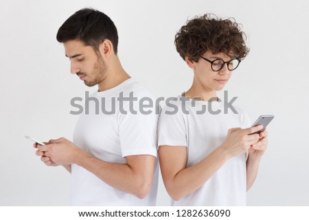 Unhappy couple ignoring each other using mobile phones. Boyfriend and girlfriend with smartphone addiction isolated on gray. Bad relationship concept