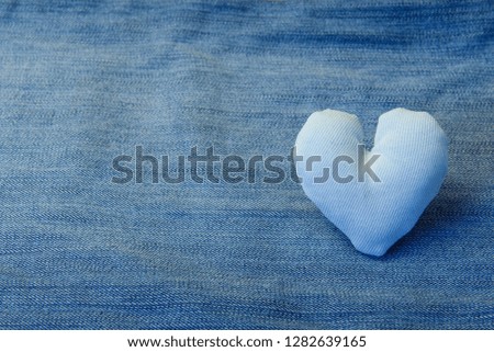 A white fabric heart lies on a denim background,