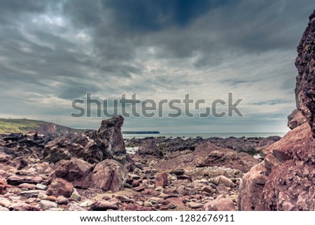 Beautiful scenery of Pembrokeshire coastline,South Wales,Uk.Rock formations on beach exposed during low tide and moody sky over horizon.Scenic landscape of british coast.Nature image with copy space.