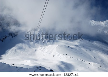 Steel ropes of elevator against snow glacier slope, white clouds and peaks of the Alps, Mont Blanc, France