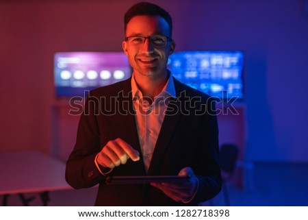 The happy man in glasses working with a tablet in the dark room