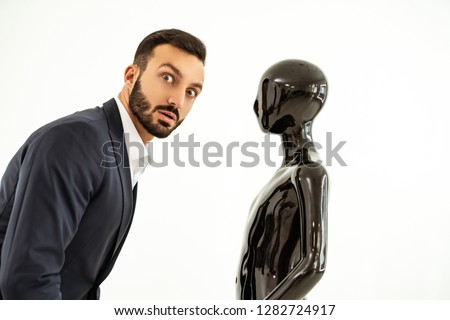 The surprised businessman standing near the black dummy on the white background