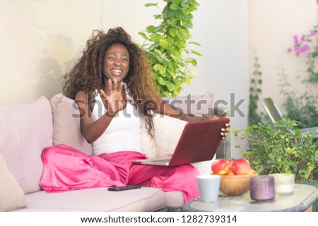 Beautiful African American, Black young Woman with crazy curly hair, wearing a bright pink pant on her laptop computer sitting outside in her patio sofa  drinking coffee or tea on a bright sunny day