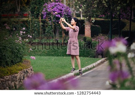 Asian girl using smartphone to take pictures in flower garden