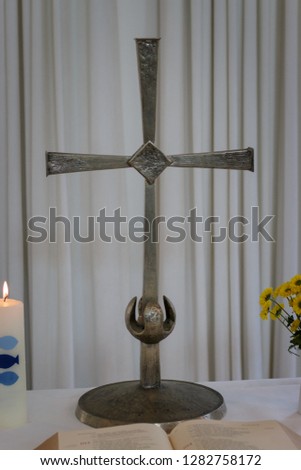 Small altar with holy cross, open bible, burning baptism candle and flowers in a vase