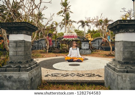 Young woman practicing yoga - meditation in the tropical garden with yin yang sign.