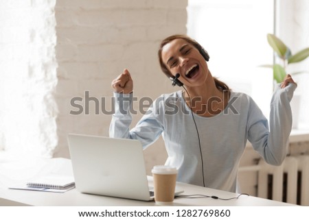 Joyful woman in headphones using laptop, sing and dancing during break, moving in rhythm with favorite music, happy female in headset enjoying, studying online, e-learning
