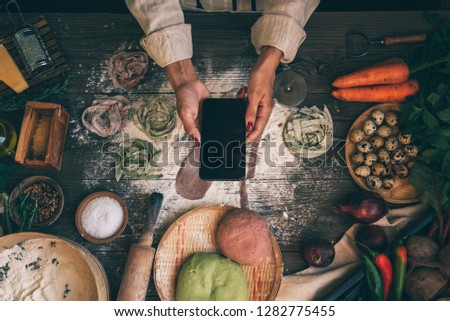 Hands with the smart phone pictures of meal. Young woman, cooking blogger is cooking at the home kitchen and is making photo at smartphone. Instagram food blogger workshop concept.