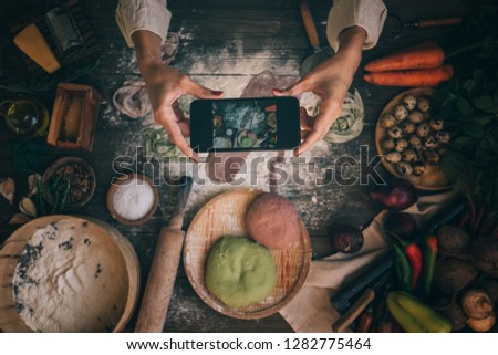 Food blogger concept. Young woman recording video on smartphone at kitchen. Woman recording every step of cooking process for her blog. Diet, technology, health, food, cooking, culinary, and people.