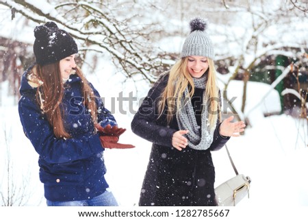 funny and happy two beautiful girlfriends play in the snow in winter, a lot of snow and winter clothes. blonde and brunette emotions.